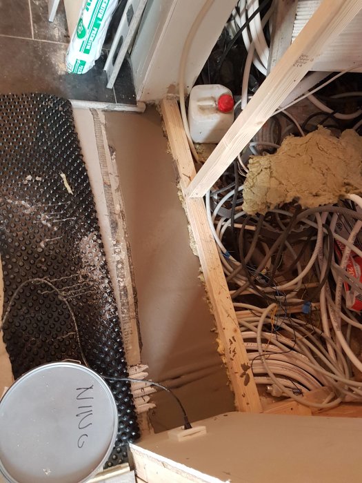 Pågående renovering med grovspacklat golv och vägg samt nyligen lagd matta, med synliga elkablar och konstruktionsdetaljer.