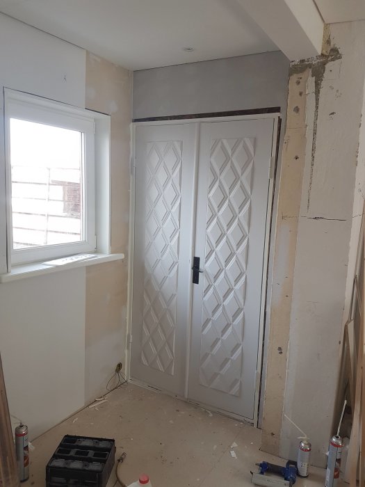 Renoveringsrum med nylagd matta, spacklade väggar och installerade pardörrar under arbete.