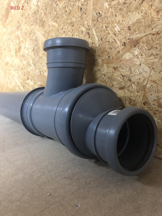 Avloppsrör reducerat från 110 till 75 mm monterat horisontellt mot en plywoodvägg, märkt som bild 2.