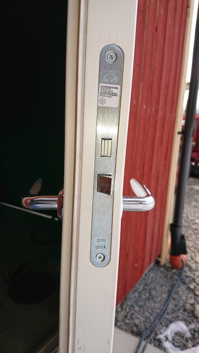 Låskista med märkningen ASSA ABLOY på en vit dörrkant med synliga låsdelar och dörrhandtag.