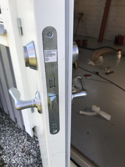 Nyinstallerad dörrhandtag och låscylinder på vit dörr med suddig byggarbetsplats i bakgrunden.