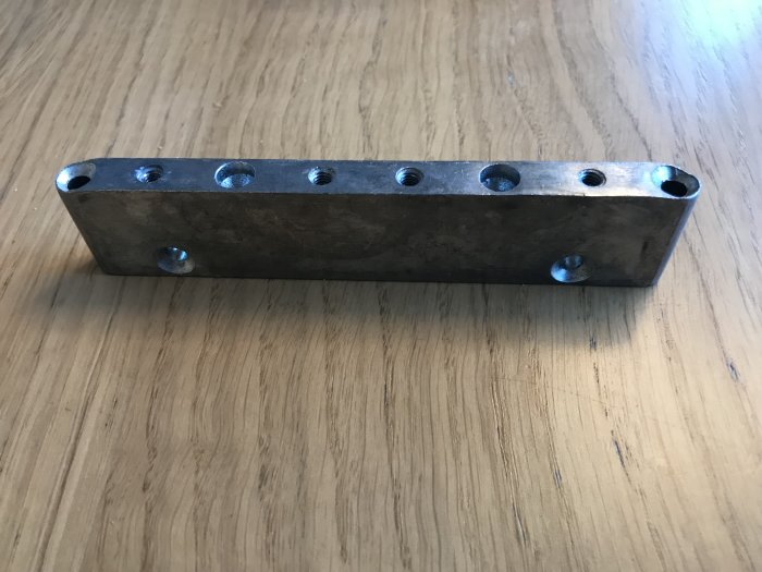 Metallbeslag med flera hål, använt för vikdörr, på ett träbord.