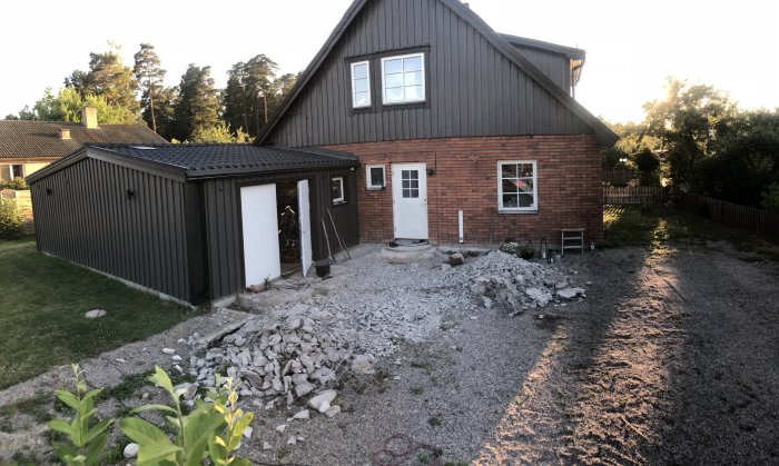 Villa med tegelfasad och planerad entrétakbyggnation, angränsande garage, byggmaterial på marken.