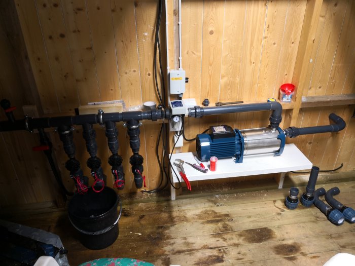 Vattenpumpsystem med flera filter och rör anslutna till en pump i ett träpanelerat rum.