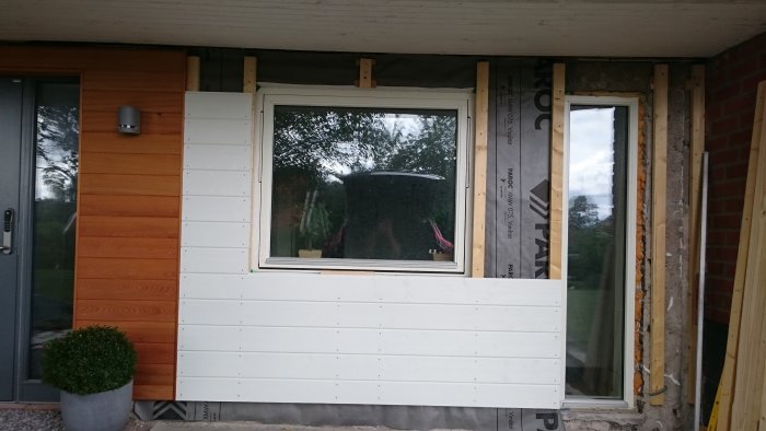 Delvis klädd fasad på hus med isolermaterial och träpaneler synlig runt fönstret.