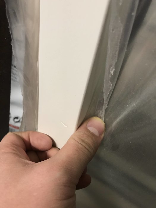 Hand som håller i en vit dörrkarm med synlig skarv mot en grå plastyta.