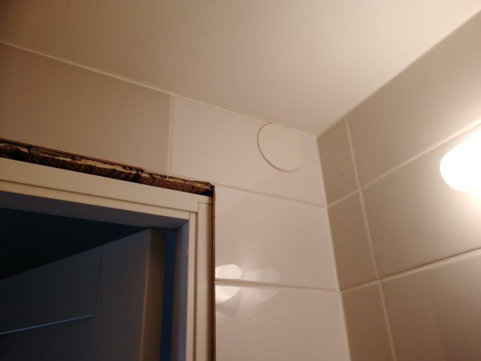 Vit kaklad vägg med olika nyanser av kakelplattor och synlig taklist.