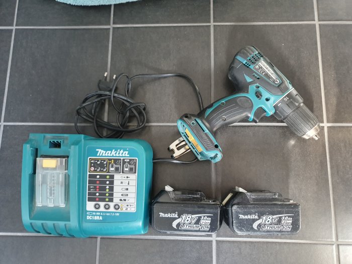 Makita borr-skruvdragare med snabbladdare och två batterier på kakelgolv, ingen förpackning.