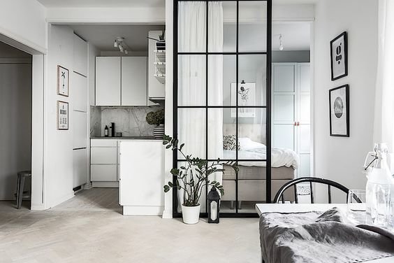 Modern studio apartment with a glass partition separating the bedroom from the living area, with minimalistic decor.