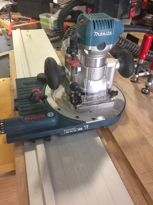 Makita fräs som fräser T-spår i en träskiva, stödd av en Bosch fräsvagga och guidad av en Festoolskena.