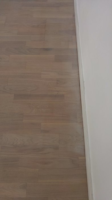 Parkettgolv med ojämn applikation av hårdvaxolja visande flammighet och vita kanter vid väggen.