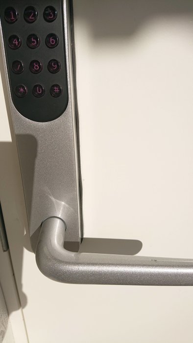 Elektronisk dörrhandtag med sifferkodspanel och låsmekanism vid en ljus dörrkant.