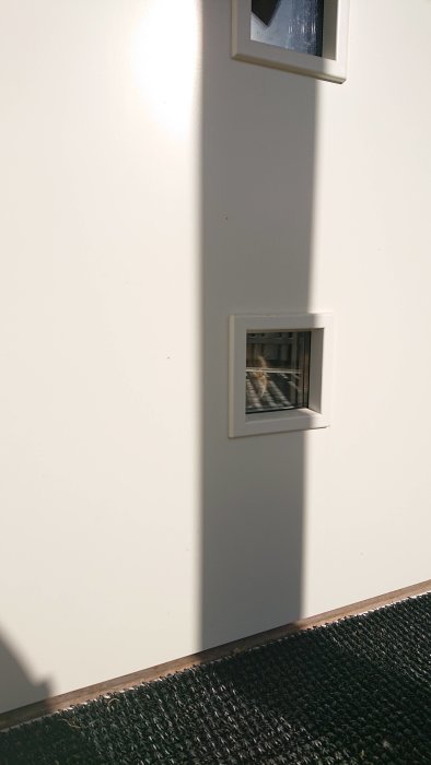Vägg med inbyggda fönster visar reflektion av byggnad, skuggor på vägg och golv.