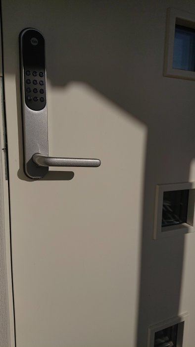 Modern ytterdörr med elektroniskt kodlås och handtag i närbild, dagsljus.