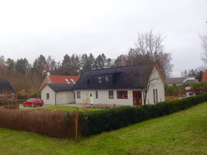 Ett nybyggt 1,5-plans villa på 92 m² plus tillbyggnad, med bil och häck framför.