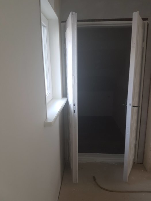 En vit dörr som är öppen men hindras från att öppnas helt av en vägg.