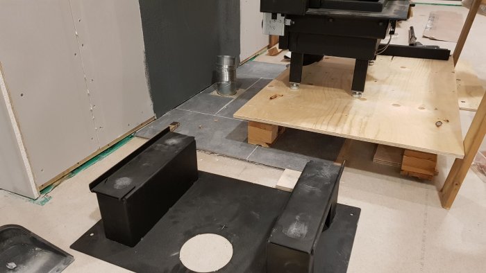 Ojämn klinkeryta med braskamins plåtfundament och ofärdigt golvarbete i rum under renovering.