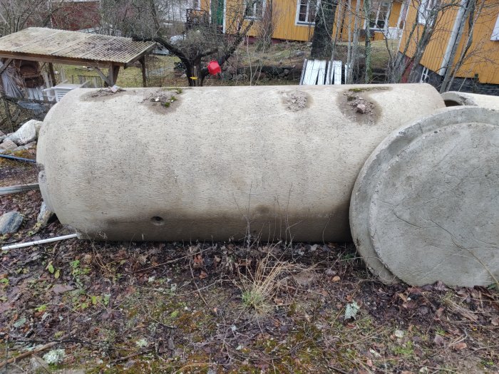 Ett stort armerat betongrör på gräs, med tecken på nötning och en liten skada på kragen.