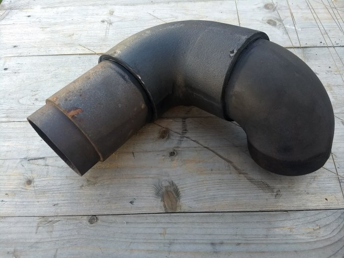 Gjutjärnsböj på träunderlag, använd för att ansluta gamla rör med synlig Sika Fireseal-tätning.