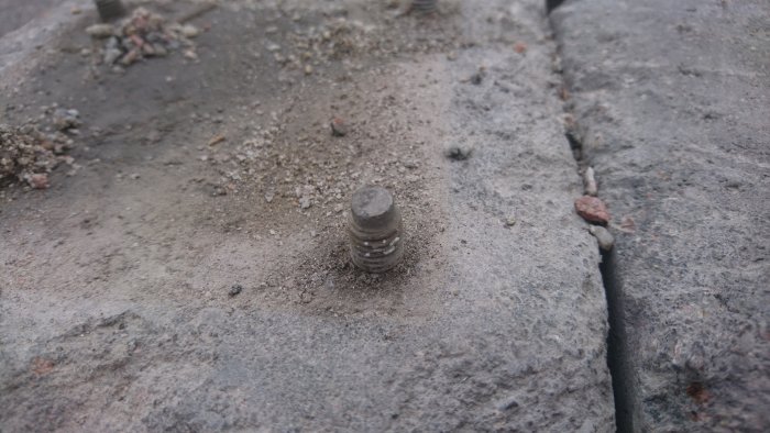 Outdoor anchor bolts on concrete, some with rust and chipped surface due to post base replacements.