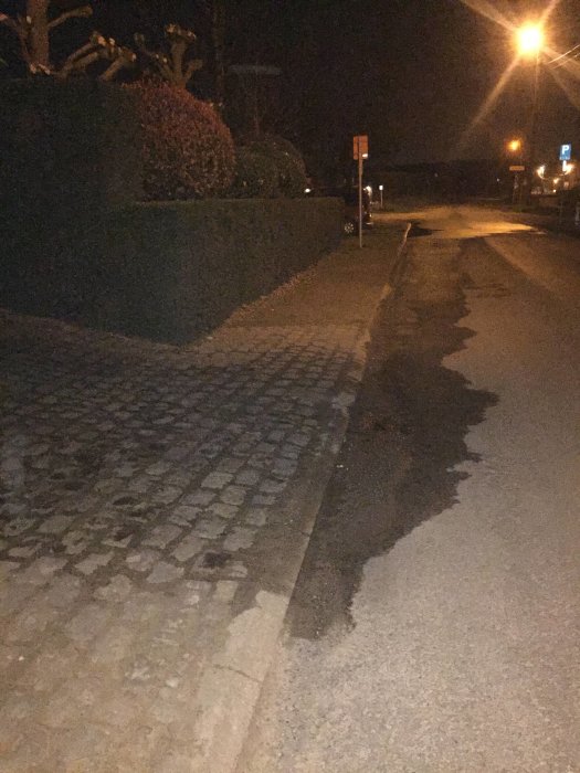 Nattlig gatubild där vatten pumpas ut och skapar en pöl längs trottoarkanten.