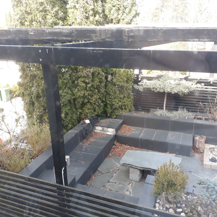 Uteplats med lossnade plattor på lecablock och omgivande trädgård.