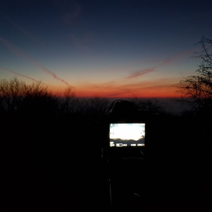 Kamera på stativ fångar en solnedgång med färgsprakande himmel i bakgrunden.