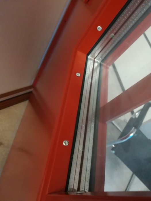 Röd dörr med stor synlig skruv och fönsterram, oväntade detaljer som bryter mot sekelskiftesstil.