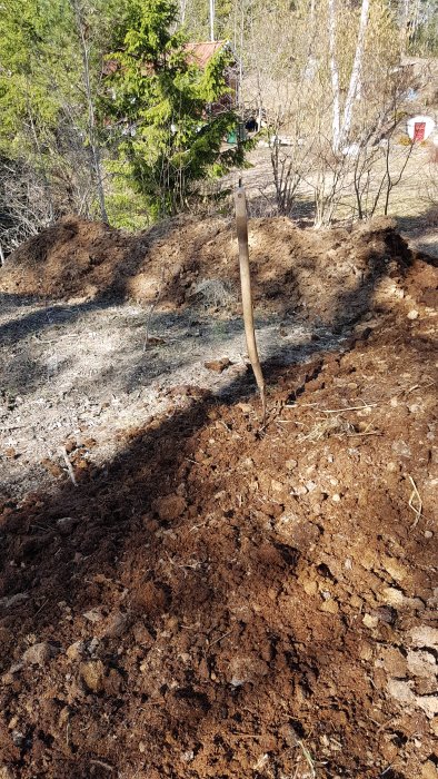 Jordhög med hästgödsel och grusig fyllnadsmassa på en tomt med spade i förgrunden.