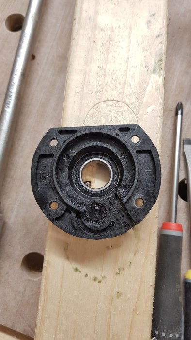 Svart plastkomponent från Ryobi cirkelsåg med inbyggt kullager på träplanka.