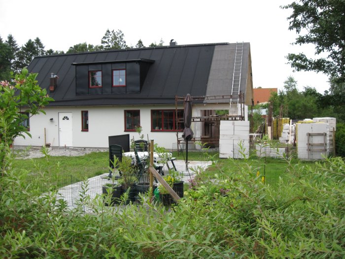 Hus under renovering med en tillfällig brun vägg skymtande inomhus, material och byggställningar synliga utanför.