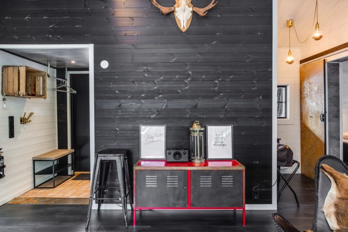 Modernt inrett rum med svart väggpanel, röd sideboard och djurkranium, stämningsfull belysning.