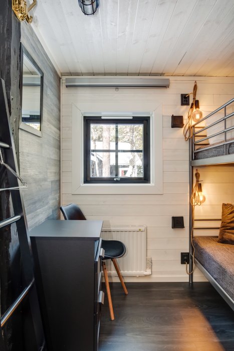 Välupplyst liten stuga interiör med loftsäng, skrivbord, fönster och modern belysning.