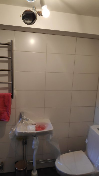 Renoverat badrum med öppet elektriskt arbete i taket, handfat skyddat med plast och synlig toalett.