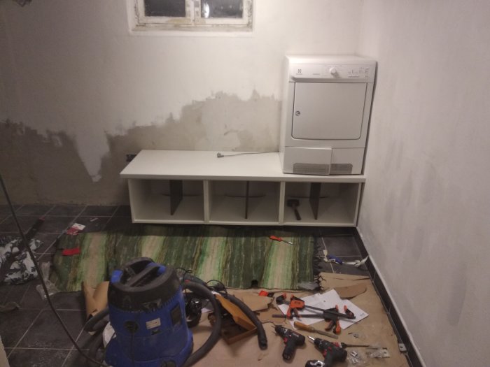 Orenoverat utrymme med omonterad möbel, torktumlare och verktyg på golvet.