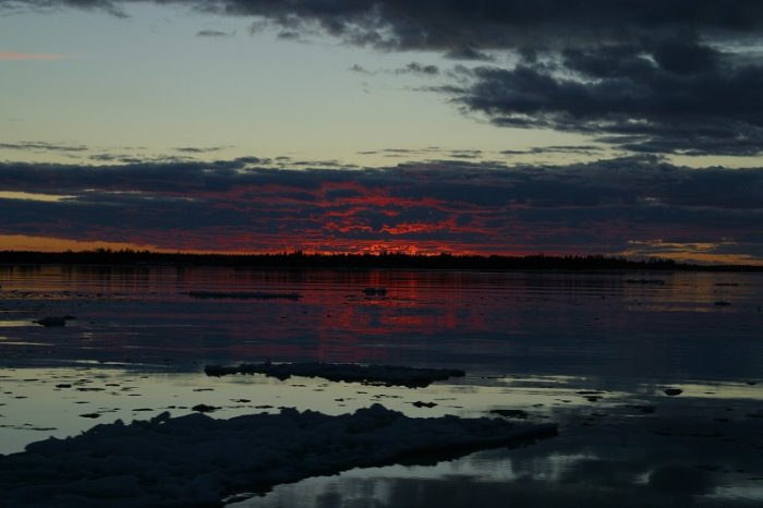 Solnedgång över en isig skärgård med delvis öppet vatten och moln på himlen.