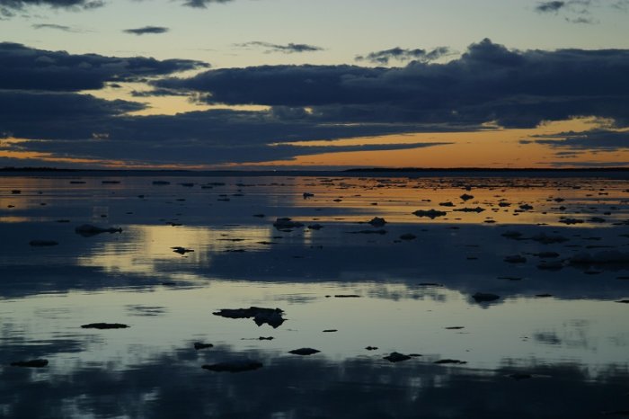 Skärgårdsutsikt med isflak på vatten vid solnedgång, reflekterande himmel och lugnt hav.