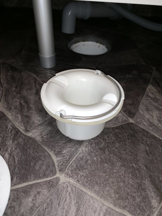 Nytt vattenlås i tvättstuga, kopplat till gråa avloppsrör, bredvid öppen golvbrunn.