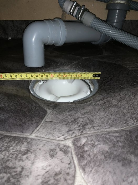 Nya vattenlås synliga på brunnen i tvättstuga, mätband över brunnen visar dimensioner, på stenplattsgolv.
