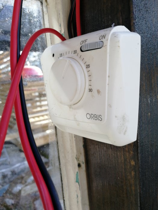 Gamla termostat kopplad till väggen omgiven av röda kablar, med inställningsratten på.