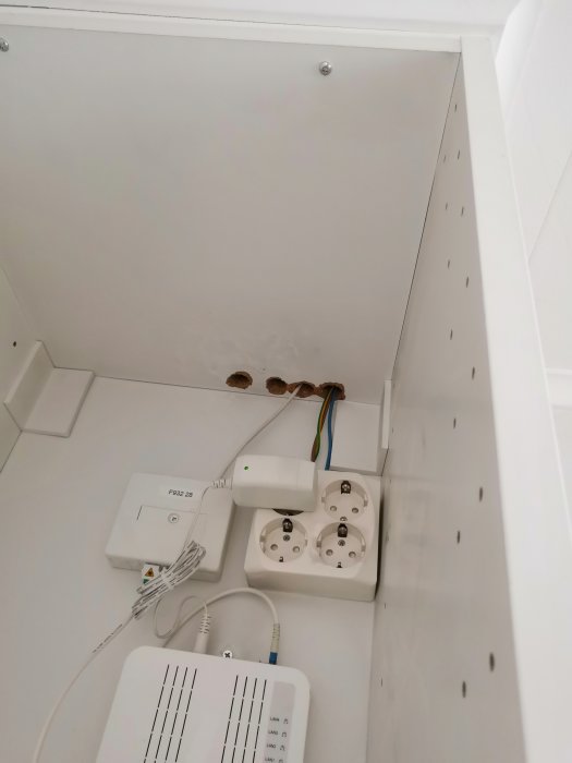 Översikt av ett öppet elskåp med en router, dubbeluttag och oisolerade kabelgenomföringar som leder uppåt.