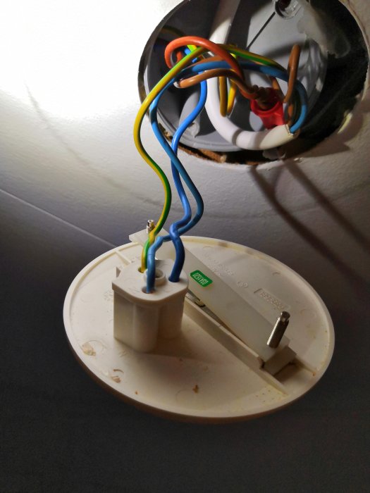 Öppet lamputtag med felaktigt kopplade färgkodade ledningar, två blå synliga, utan skyddande kåpa.
