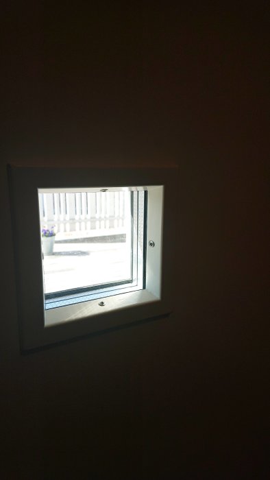 Liten vit fönsterkarm från insidan med ljus som strömmar in och en mörk omgivning.