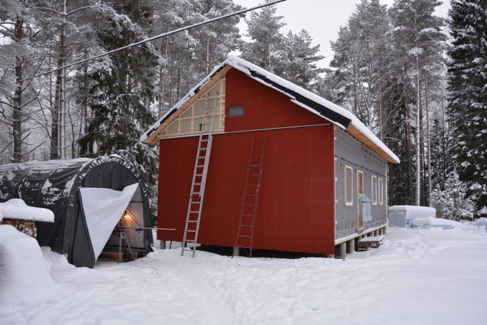 Hus under renovering med ny panel på en gavel, snötäckt mark och en stege lutad mot huset.