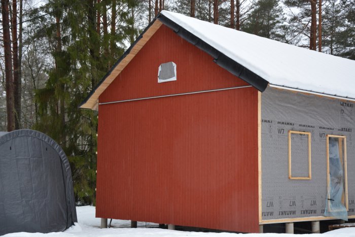 Hus under renovering med röd panel på ena gaveln, isolering på andra sidan i vintersnö.