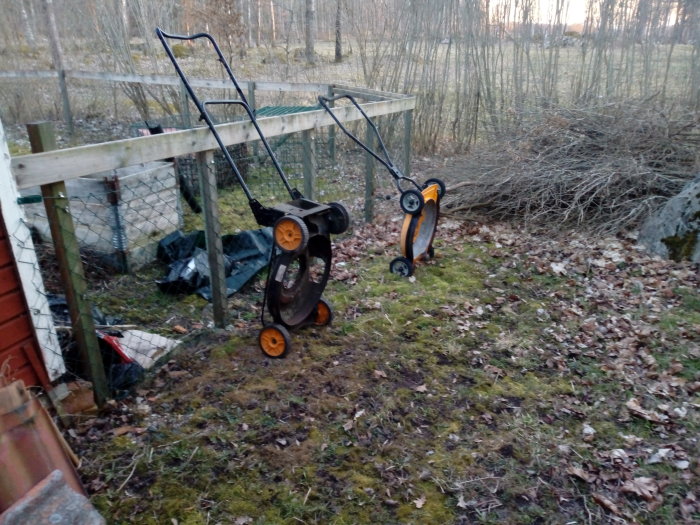 Två gräsklipparunderreden utan motorer står i en trädgård med skog i bakgrunden.