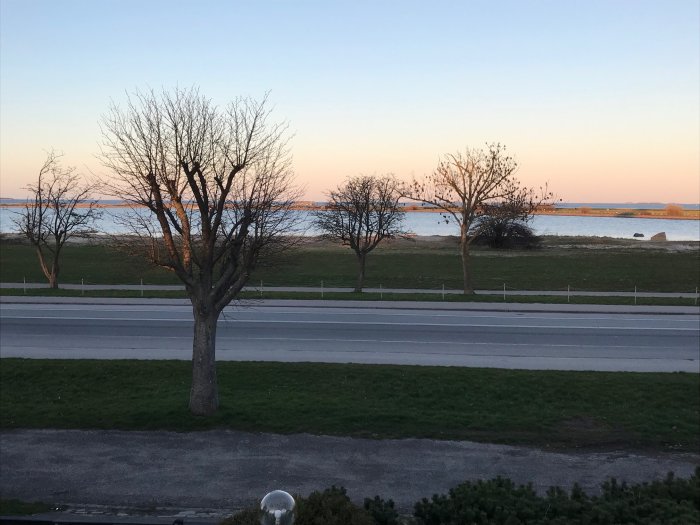 Utsikt över Öresund med trafikerad väg i förgrunden och Öresundsbron i bakgrunden vid skymning.