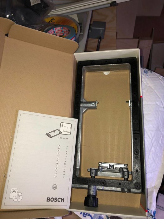 Ny oanvänd slipram till Bosch bandslip i kartong, vid sidan av Bosch bruksanvisning.