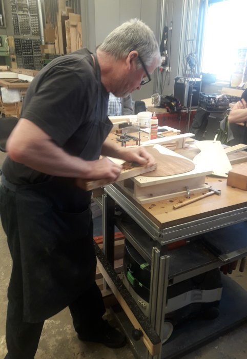 Person arbetar med träslöjd på en arbetsbänk i en verkstad.