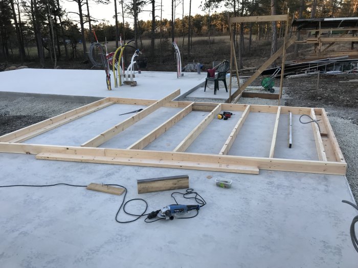 Nyuppreglad trästomme för hus på gjuten betongplatta med verktyg och byggmaterial synliga.